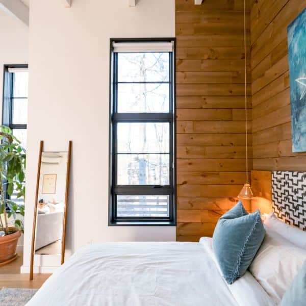 Modern vacation rental bedroom with natural wood accent wall, bright windows, and freshly made bed